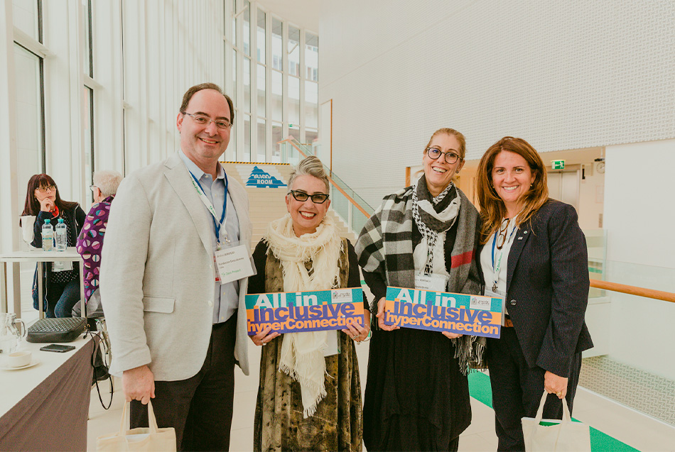 Fotografia colorida, Claudia Werneck e Rosana Fonseca com os parceiros da Fundacíon Descubreme. Elas  representam a Escola de Gente segurando um cartaz de "All in - inclusive".