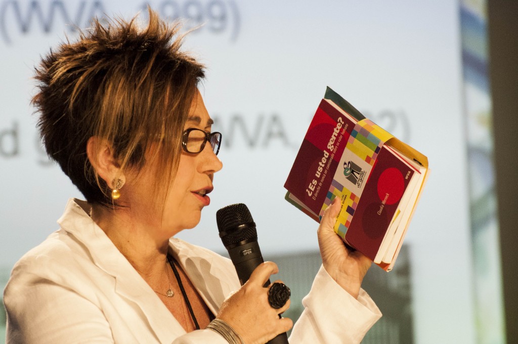 Foto mostrando Claudia Werneck, ao microfone, segurando um livro.