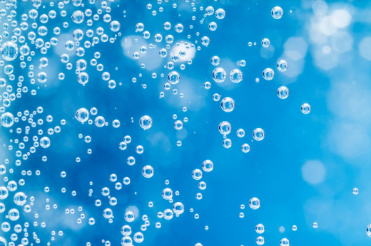A imagem mostra o que parece ser um recipiente com água. O fundo é azul, e pequenas bolhas de ar aparecem em primeiro plano.